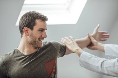 Genç yakışıklı beyaz adam kolunu yardım doktoru ile germe.