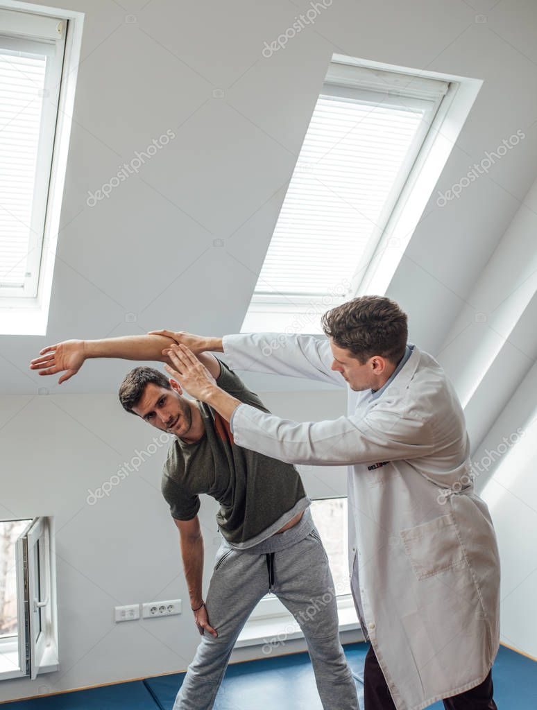 Young patient stretching his arm with his physician helping.