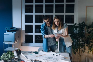 İki genç Kafkas tasarımcıları, bir erkek ve bir kadın, birlikte geceleri bir ofiste çalışırken tablet kullanma.