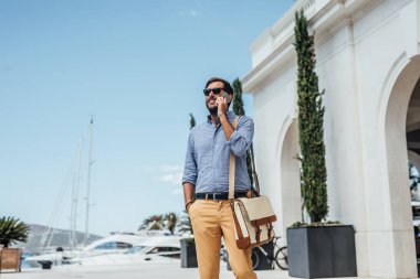 Limanda yürüyüş ve cep telefonuyla konuşurken yakışıklı işadamı.