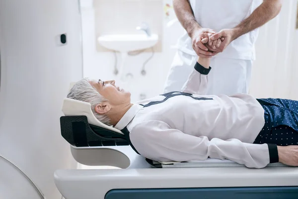 医疗技术人员牵着躺在 扫描仪床上的一名老年妇女的手 — 图库照片
