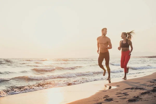 ハンサムな白人男性と夕日の砂浜ビーチを走る美女 ロイヤリティフリーのストック画像