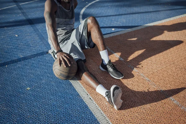 坐在室外篮球场上拿篮球的年轻男子 — 图库照片