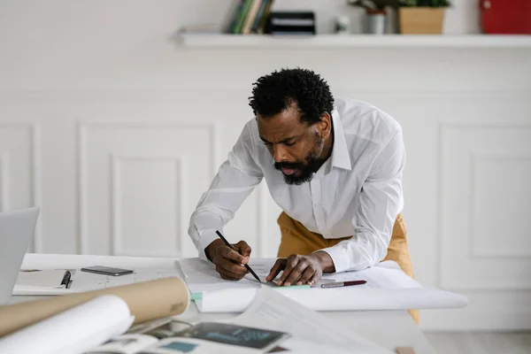 认真的非洲人建筑师绘制图纸在他的办公室 图库照片