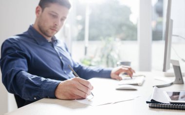 Genç işadamı modern ofis alanı, bir masaüstü bilgisayarda çalışırken not alma.