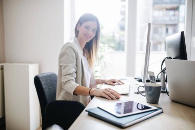 Bir fare ve klavye modern ofis alanı kullanan bir masaüstü bilgisayarda çalışan genç iş kadını.