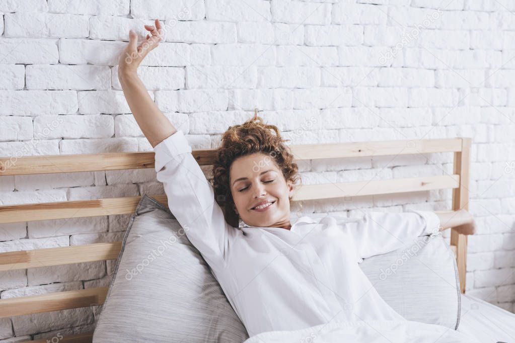 Beautiful smiling Caucasian woman waking up and stretching in her bed.