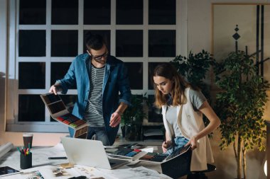 İki genç Kafkas sanatçı, bir erkek ve bir kadın ofiste geceleri birlikte çalışırken halı renk paletleri incelenmesi,.