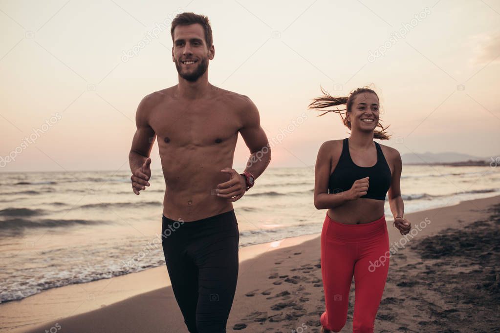 Beautiful smiling woman and handsome man running on sandy beach in sunset.