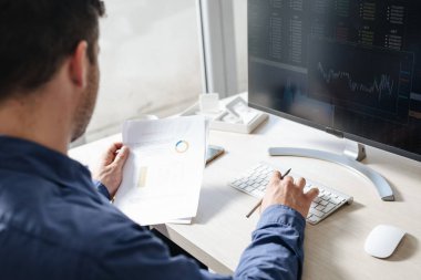 Genç işadamı komisyonculuk şirketinde bir masaüstü bilgisayarda çalışırken onun notlar okuma.