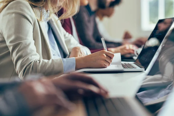 Hands of the unrecognizable business people typing on their laptops and writing notes at the modern office space.