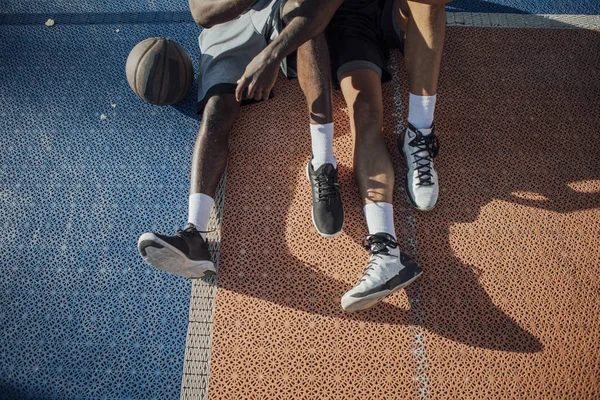 Piernas Los Dos Jóvenes Hombres Irreconocibles Sentados Una Cancha Baloncesto —  Fotos de Stock