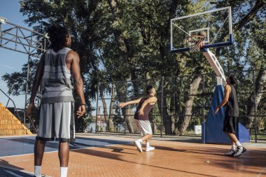 Basketbol oynarken bir açık basketbol sahası üzerinde üç genç adam.