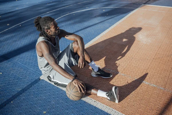 坐在室外篮球场上拿篮球的年轻人 — 图库照片