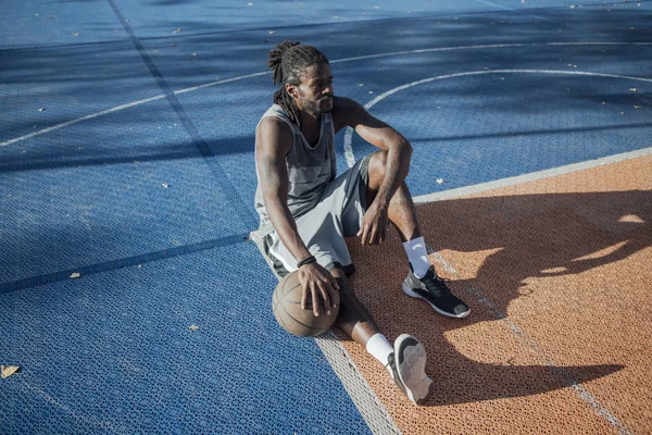 坐在室外篮球场上拿篮球的年轻人 — 图库照片