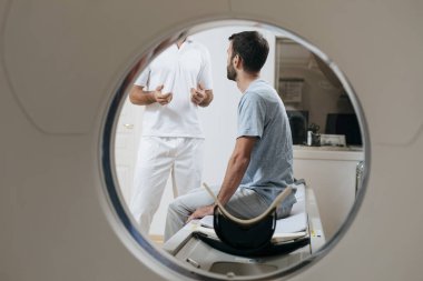 Ayakta ve onun hasta için Ct tarayıcı yatakta oturup konuşurken tanınmaz halde tıbbi teknisyen.