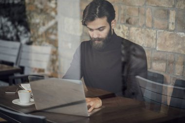 Kahve dükkanında oturmuş ve dizüstü bilgisayarda yazarak yakışıklı beyaz adam.