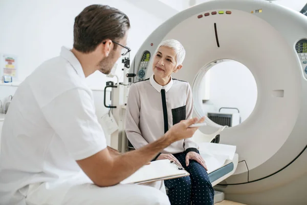 Young Doctor Talking Senior Woman Taking Notes While Sitting Scanner — Stock Photo, Image