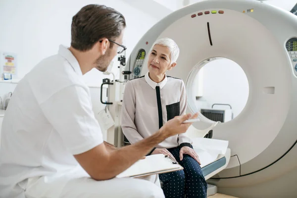 Jovem Médico Conversando Com Uma Mulher Idosa Tomando Notas Enquanto — Fotografia de Stock