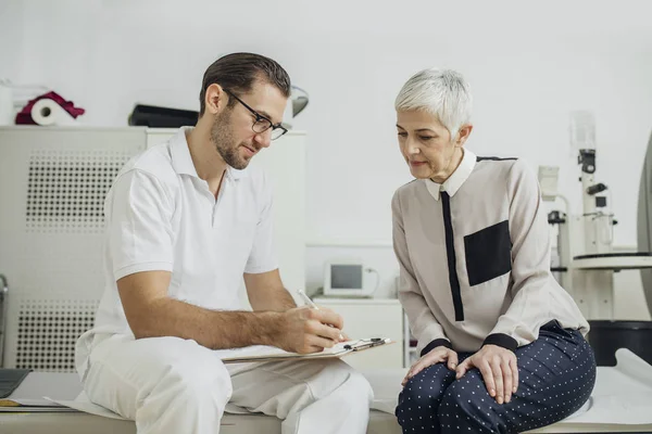 Jovem Médico Conversando Com Seu Paciente Tomando Notas Enquanto Sentado — Fotografia de Stock