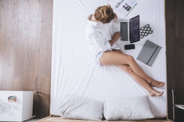 Genel gider bir yatakta yatarken onu laptop kullanarak beyaz kadın fotoğrafı.