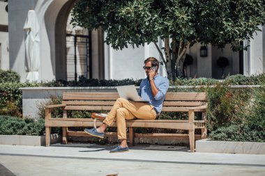 Açık havada oturma ve cep telefonuyla konuşurken yakışıklı beyaz işadamı serbest meslek.