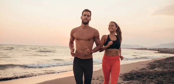 美丽的微笑的女人和英俊的男人在日落在沙滩上奔跑 — 图库照片