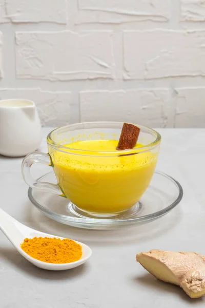 Cup of turmeric golden milk with milk cane, turmeric powder and ginger root on concrete table. Image with copy space, selective focus