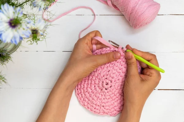 Directly above view of woman hands holding crochet hook and crocheting with ribbon yarn