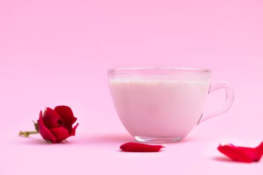 Pastel pembe arka planda cam bir fincanda pembe ay sütü ve metin için yer.