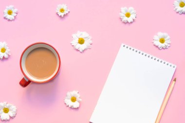 İçinde kahve fincanı, kalem ve pastel pembe arka planda çiçekler olan boş bir defter. Yaz ya da bahar kompozisyonu