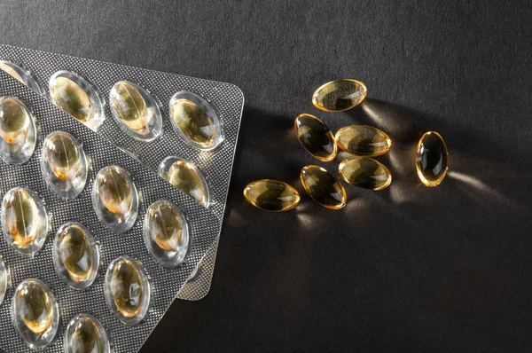 Fish oil capsules and blister on dark background — Stock Photo, Image