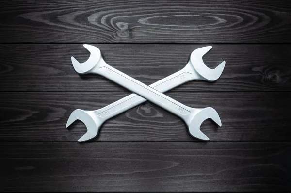 stock image Crosshair of two chrome wrenches on dark wooden workbench.