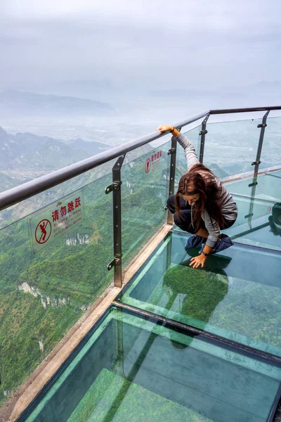 Unga kaukasiska vit kvinna knästående på glas Sky Walk på Tianmen Mountain, Zhangjiajie — Stockfoto