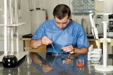 Orta yaşlı erkek laboratuvar teknisyeni laboratuarda pipette kimyasal sıvı çözeltisi test ediyor.