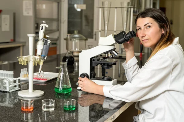 Middle age female laboratory technician sitting next to compound microscope