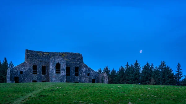Montpelier Tepesi 'nde mavi gökyüzü ve ay ile gece sahnesi. Eski, harap olmuş ve terk edilmiş Dublin, İrlanda binasının manzaralı Hell Fire Club olarak bilinir.