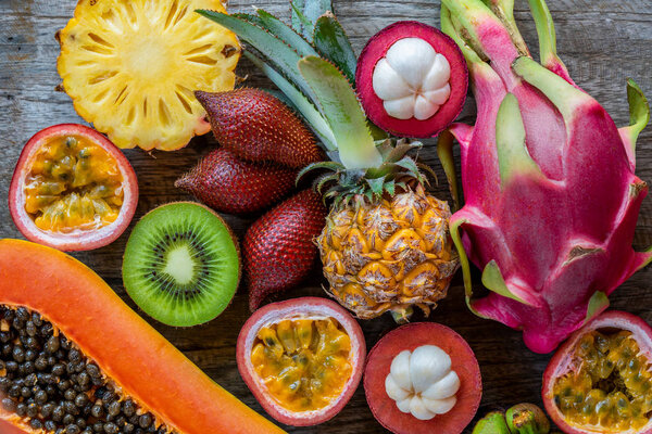Fresh exotic tropical fruits - dragon fruit, kiwi, snake fruit (salak), pineapple, mangosteen fruit, passion fruit (maracuya) and papaya on the wooden background. Fresh fruits composition, top view 