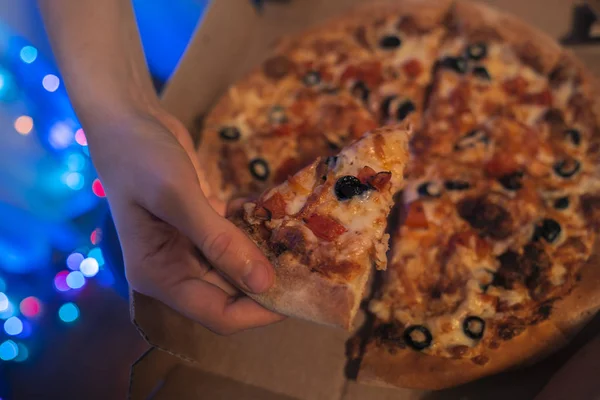 Woman\'s hand taking a piece of pizza from just delivered pizza box with blue bokeh background