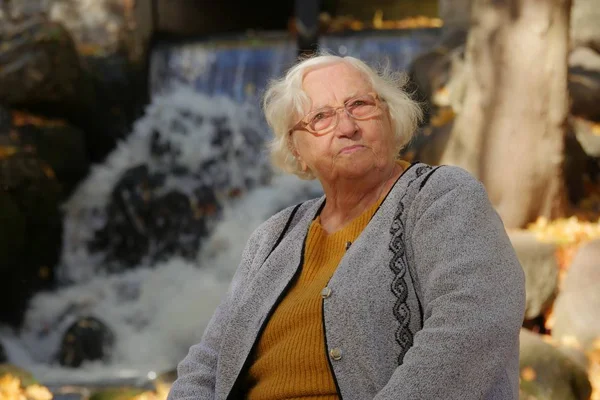 Portrait of an old lady in autumnal scenery. Waterfall in the background