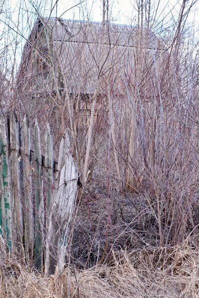Velha casa abandonada atrás de uma cerca de madeira quebrada — Fotografia de Stock
