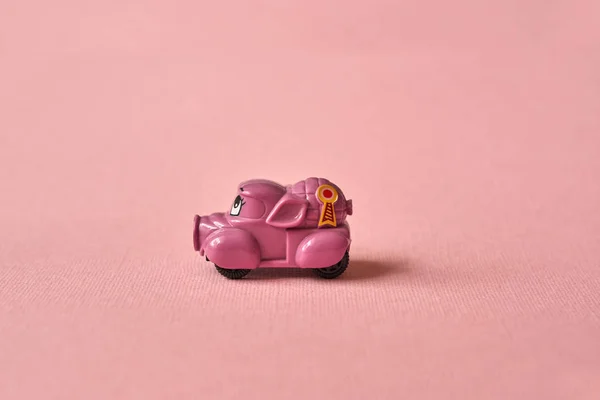 Pink toy car delivering products on a pink background. Postcard February 14, Valentine's Day. Flower delivery.