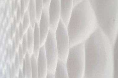 Dalgalı bir dokusu olan beyaz bir duvar. Geometrik desenli alçı taşı panelleri. Tarafsız renklerde kabartmalı duvar. Düzenli tekrarlanan hücreler. Taştan yapılmış dekoratif panel. Kabuğun dokusu..