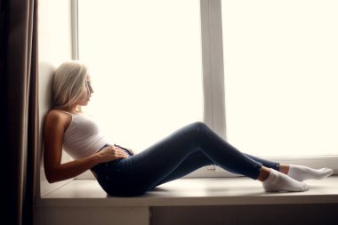 Studio narural ışık ile büyük penceresinin pencere üzerinde oturan Jeans sarı saçlı kadın moda fotoğraf güzel uygun