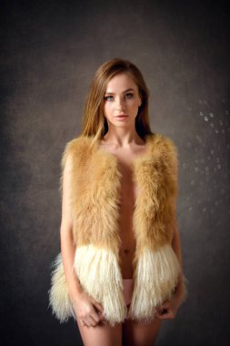 moda fotoğraf Studio gri arka plan üzerinde poz bej kürk yelek esmer saçlı güzel kadın. İhale atmosfer ateş. 