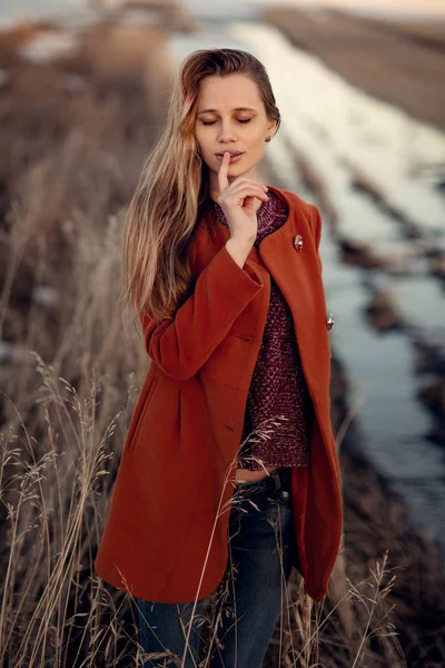 Schöne Frau mit blonden Haaren im roten Mantel, die auf einem sonnigen — Stockfoto