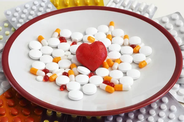 red heart, vitamins and tablets of different colors and sizes on a plate next to the pills in the package. concept pills and vitamins for the heart. Copy space.
