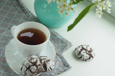 Bir fincan çay, çikolata parçalı kurabiyeler ve pencere eşiğinde kuş kirazı dalları olan bir vazo..