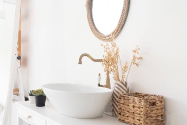 Parlak banyo, lavabo, mikser, ayna, hasır sepet ve çiçekler beyaz dolapta.
