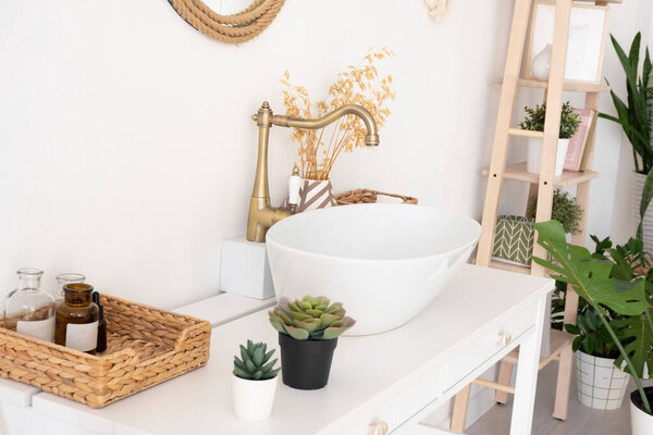 bright bathroom, sink, mixer, mirror, wicker basket and flowers on a white cabinet